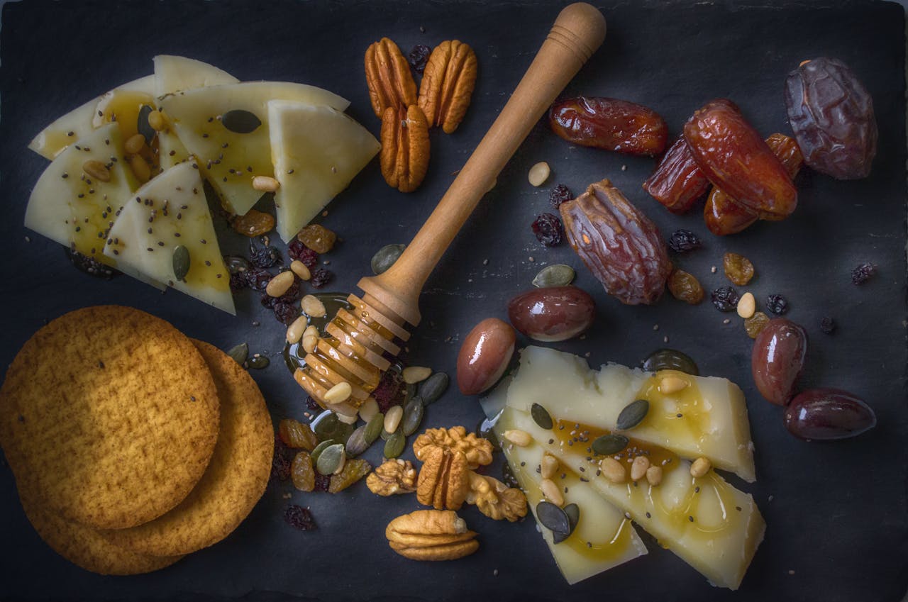 services-03 A delightful snack assortment with cheese slices, nuts, dates, and honey on a slate board.